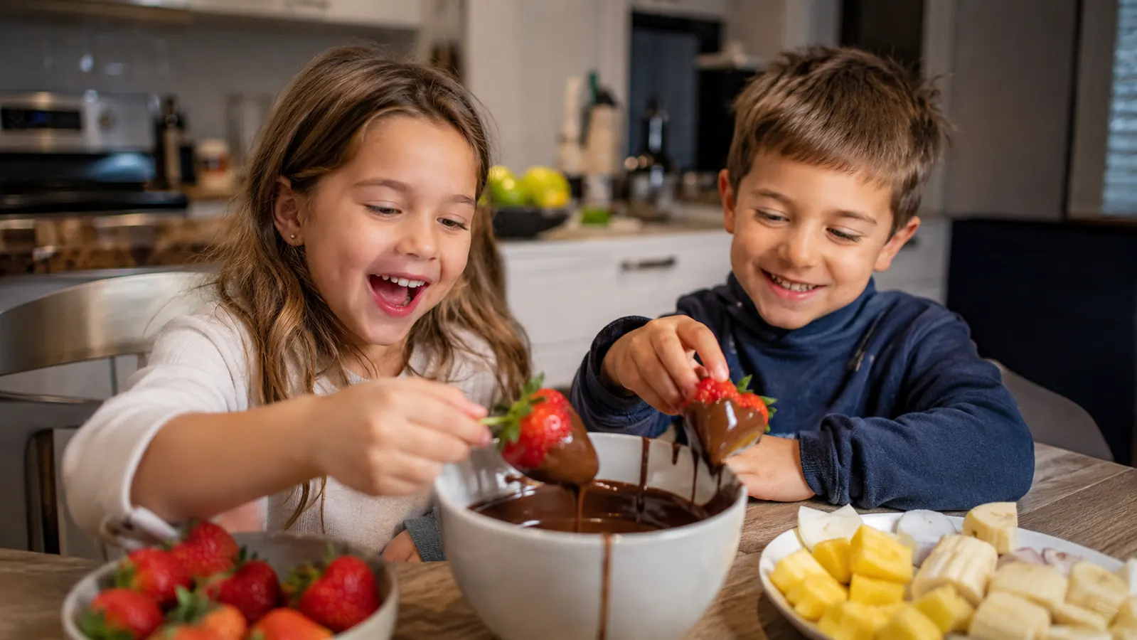 Grandkids laughing while dipping strawberries and marshmallows into chocolate fondue
