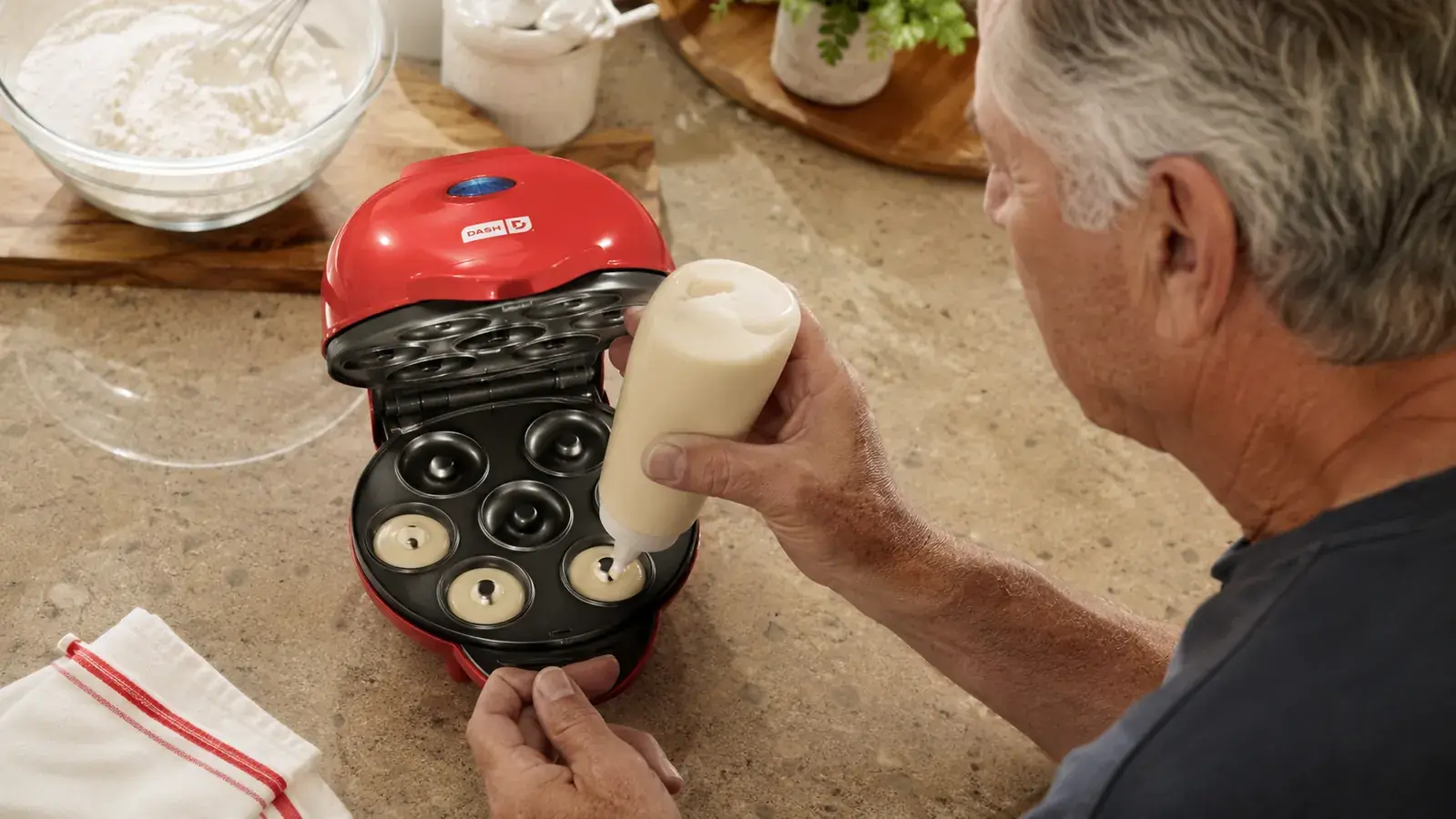 Hands pouring donut batter from a piping bag into the Dash Express Mini Donut Maker