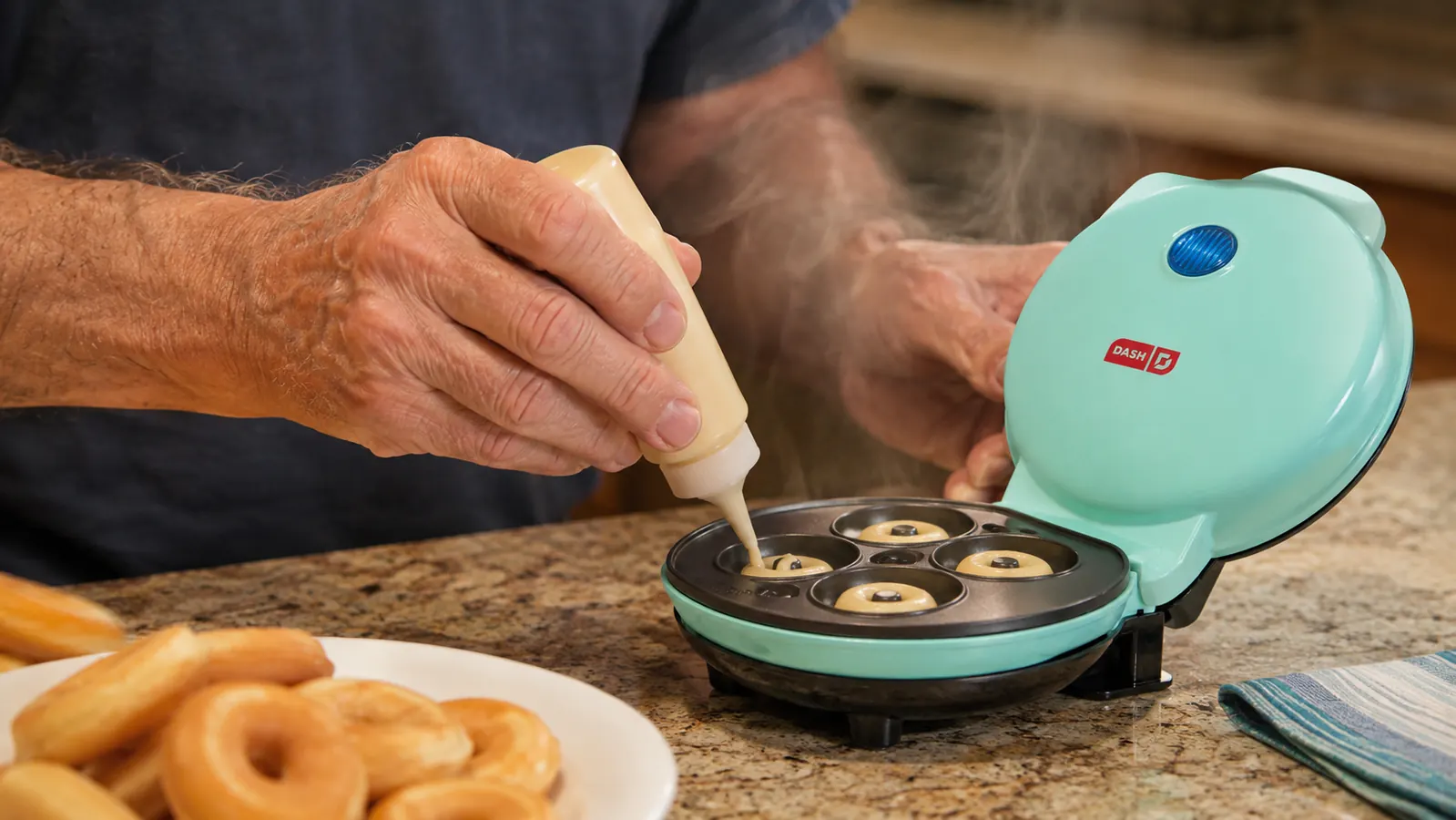 Hand pouring batter into the well of a mini donut maker with a squeeze bottle