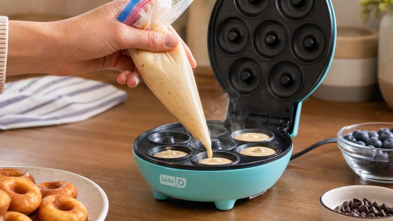 Hand piping donut batter into the wells of a Dash Express Mini Donut Maker