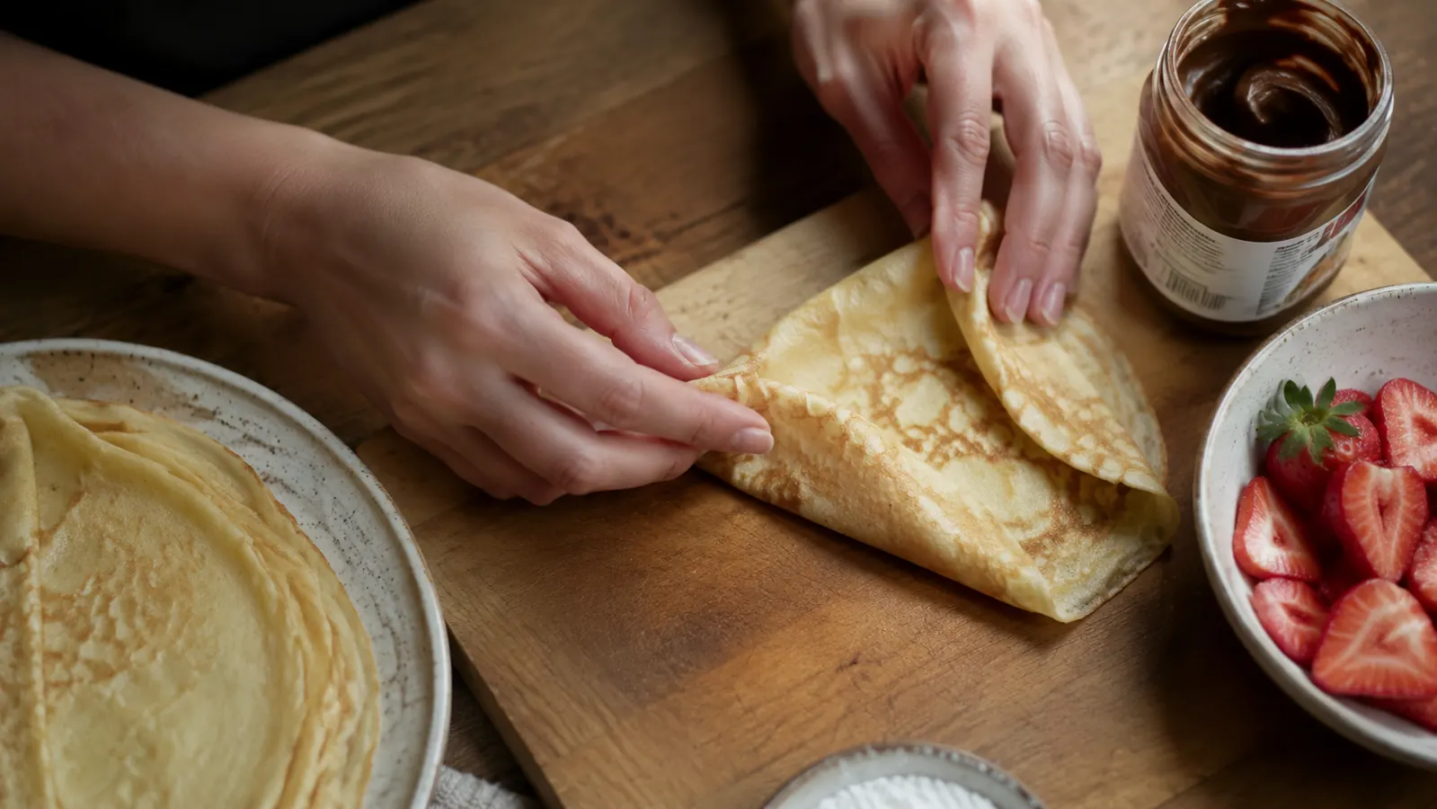 A finished crepe being folded into quarters on a cutting board with a small spatula