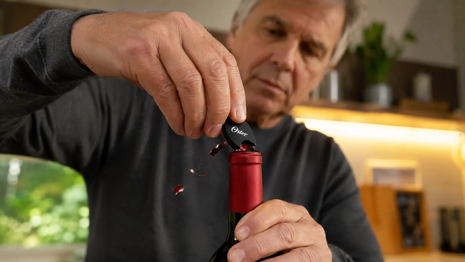 Hand pulling the foil cutter attachment off the top of a wine bottle after a couple of turns